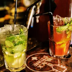 Deux cocktails rafraîchissants, un mojito vert et un autre rouge, sur un plateau en bois gravé.