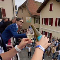 Une femme filme la plus grande bouteille du monde, d'où l'on verse du champagne dans un verre, devant une foule en liesse.
