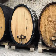 Trois fûts en bois de chêne, certains foncés, d'autres clairs, alignés dans une cave à vin.