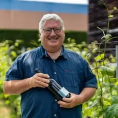 Un vigneron souriant tient une bouteille de vin dans les vignes du domaine du Trapadis.