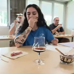 Jeune femme aux tatouages participe à une formation vin, dégustant une bière artisanale avec des accompagnements.