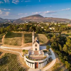 Vue aérienne du **château de Bellet**, avec ses vignobles en terrasses, son église et les collines niçoises en arrière-plan.