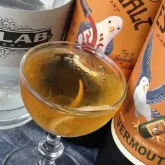 Un cocktail martini doré, garni d'un zeste d'orange, est prêt à être dégusté, entouré de bouteilles de gin et de vermouth.