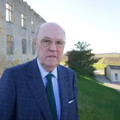 Alexandre de Lur Saluces, un homme d'affaires distingué, pose devant un château historique, les vignobles s'étendant à l'horizon.