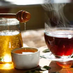 Une boisson eau et miel fumante, avec un pot de miel et une cuillère en bois dégoulinant.