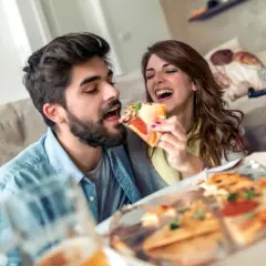 Un couple partage une pizza et de la bière, oubliant le régime pour un moment de plaisir gourmand.