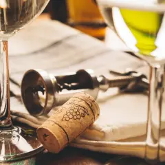 Deux verres de vin blanc, un tire-bouchon et un bouchon orné de grappes de raisin. Le droit de bouchon prix est souvent discuté lors de dégustations.