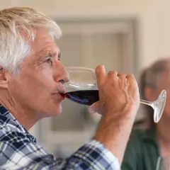 Un homme âgé boit du vin rouge. Attention, le vin périmé présente un danger.