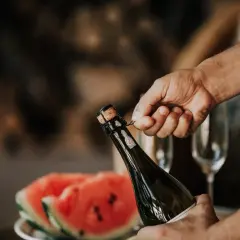 Main tenant du goulot, une main dépose délicatement le muselet. La clé pour savoir comment ouvrir une bouteille de champagne est dans ce geste précis.