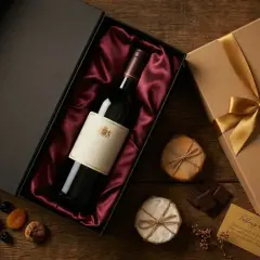 Un coffret cadeau élégant avec une bouteille de vin, des fruits secs et du chocolat, prêt à être offert par Jean-Claude Boisset.