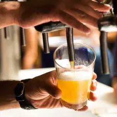Main d'un homme servant une bière blonde dans un verre. Une question se pose : pourquoi la bière donne envie de faire pipi ?