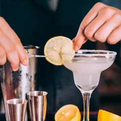 Un barman prépare un cocktail en p. avec une tranche de citron.