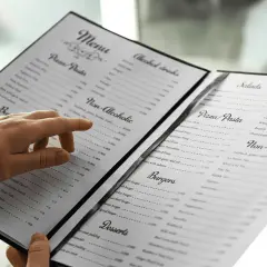 Une main parcourt le menu, cherchant le vin au verre parfait pour accompagner son repas.