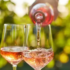 Un verre de rosé est servi dans un autre verre, sous un soleil radieux. Un moment parfait pour boire du rosé tous les jours.