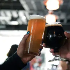 Deux mains lèvent des verres de bière, l'un blond et l'autre brun, pour un toast.
