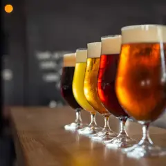 Une dégustation de différents types de bière, alignés sur un comptoir en bois. Les verres présentent des couleurs allant du blond doré au brun foncé, avec une mousse crémeuse.