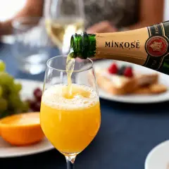 Un cocktail à base de champagne est versé dans un verre, avec des fruits frais et des viennoiseries en arrière-plan.