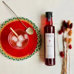 Un verre de boisson pétillante avec de la bière et de la grenadine, une bouteille de sirop de grenadine Lissip et des fleurs séchées.