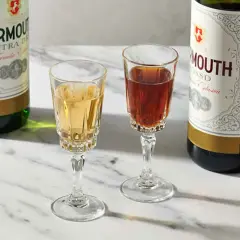 Deux verres de vermouth blanc et rouge, accompagnés de leurs bouteilles. Un apéritif raffiné.