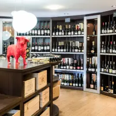 Cave à vin avec étagères remplies de bouteilles, une statue de taureau rouge et des bouteilles de champagne au premier plan.