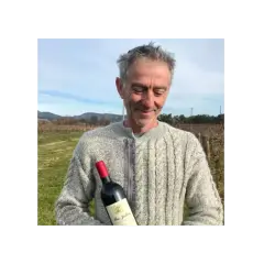 Un homme souriant tient une bouteille de vin Mas Jullien dans un vignoble.