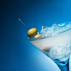 Un cocktail gin martini glacé, avec des olives sur un cure-dent bleu, sur fond bleu dégradé.