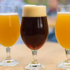 Trois verres de bière, deux blondes et une brune, sur une table en bois. Une dégustation pour comparer le goût et le calorie biere.