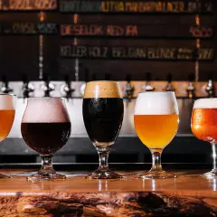Cinq verres de bière, dont une pale ale ou ipa, sur un comptoir en bois. Derrière, des tireuses et un tableau des bières.