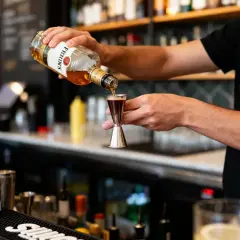 Un barman verse du whisky d'une bouteille dans un doseur. Il prépare un cocktail, prêt à boire à la bouteille ou au verre.