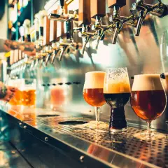 Verre de bière au bar, avec un barman en arrière-plan qui sert une chope.
