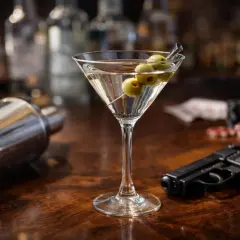 Un verre de martini, un shaker, des jetons de casino et un pistolet sur un bar en bois. L'ambiance parfaite pour un apéro James Bond.