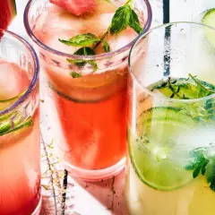 Trois verres de cocktail classique, garni de concombre, menthe et pastèque, sur un fond clair.