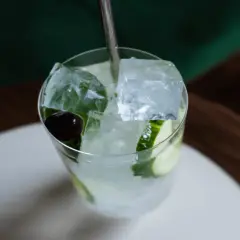 Un verre rempli de glaçons transparents, de rondelles de concombre et d'une cerise, prêt à être dégusté.