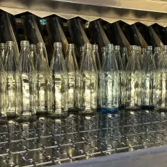 Une rangée de bouteilles en verre transparentes alignées sur une chaîne de production. On se demande combien de verre dans une bouteille d'eau.