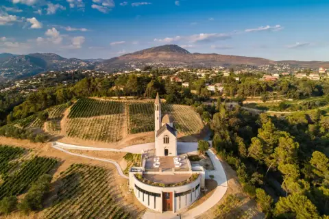 Vue aérienne du **château de Bellet**, avec ses vignobles en terrasses, son église et les collines niçoises en arrière-plan.