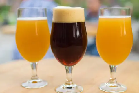 Trois verres de bière, deux blondes et une brune, sur une table en bois. Une dégustation pour comparer le goût et le calorie biere.
