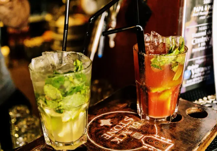 Deux cocktails rafraîchissants, un mojito vert et un autre rouge, sur un plateau en bois gravé.