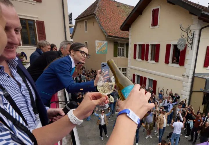 Une femme filme la plus grande bouteille du monde, d'où l'on verse du champagne dans un verre, devant une foule en liesse.