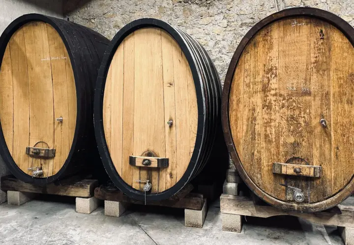 Trois fûts en bois de chêne, certains foncés, d'autres clairs, alignés dans une cave à vin.