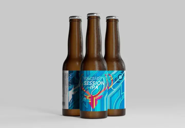 Trois bouteilles de bière ambrée, dont une avec une étiquette colorée "VOLCELEST SESSION IPA" aux motifs géométriques bleus et roses.
