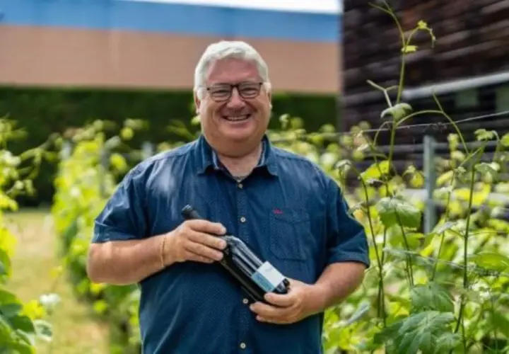 Un vigneron souriant tient une bouteille de vin dans les vignes du domaine du Trapadis.