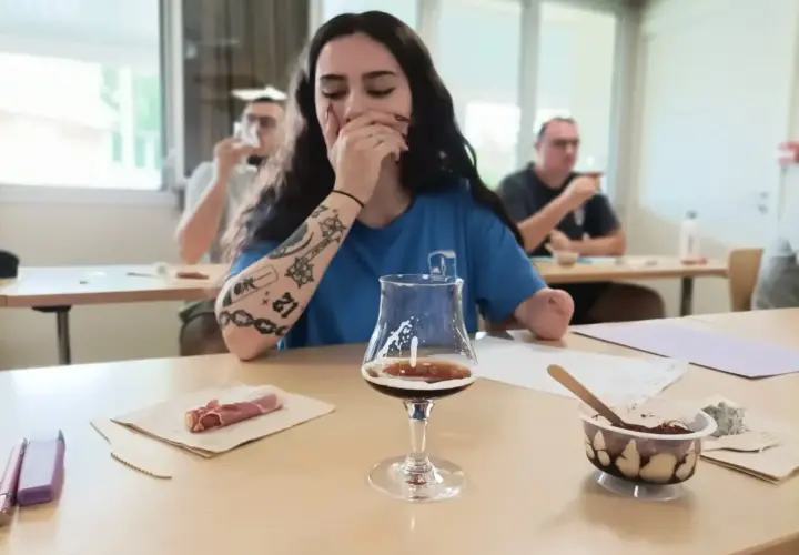 Jeune femme aux tatouages participe à une formation vin, dégustant une bière artisanale avec des accompagnements.