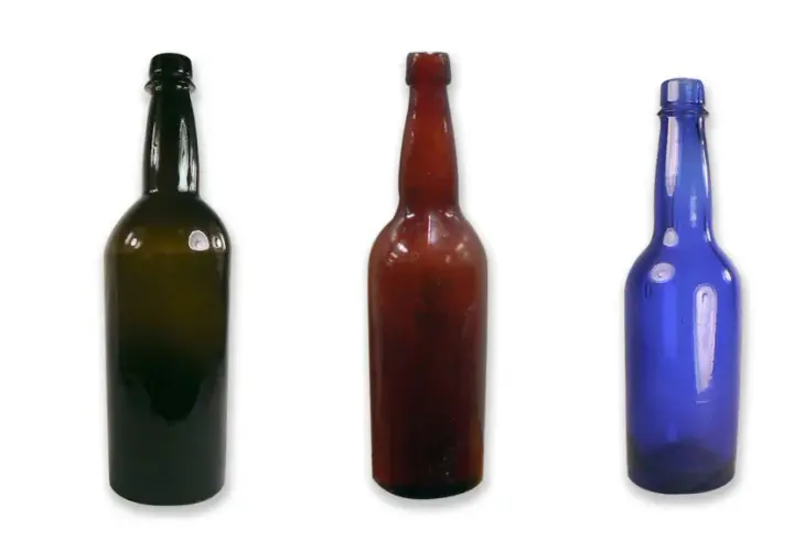 Cinq bouteilles de différentes couleurs et tailles, dont une bouteille de bière ambrée, alignées sur fond blanc.
