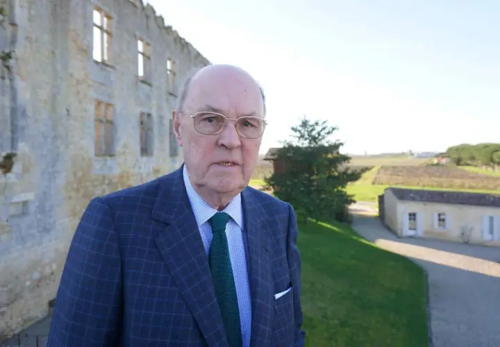 Alexandre de Lur Saluces, un homme d'affaires distingué, pose devant un château historique, les vignobles s'étendant à l'horizon.