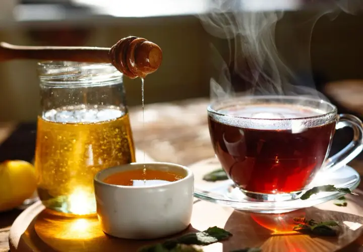 Une boisson eau et miel fumante, avec un pot de miel et une cuillère en bois dégoulinant.