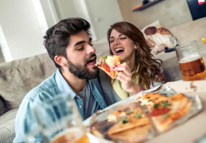 Un couple partage une pizza et de la bière, oubliant le régime pour un moment de plaisir gourmand.