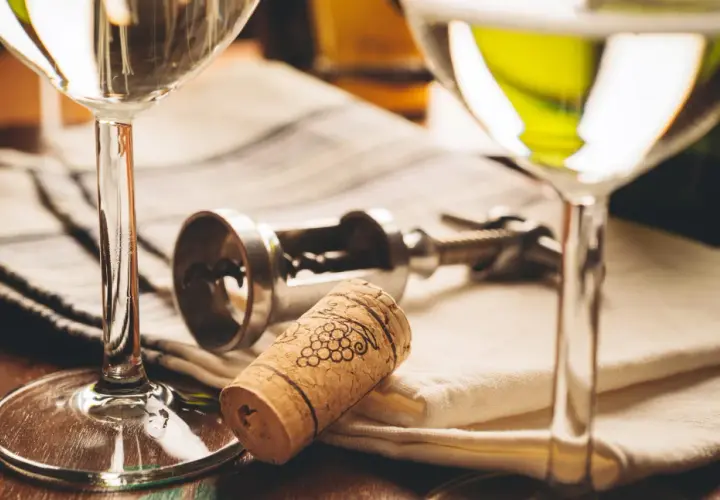 Deux verres de vin blanc, un tire-bouchon et un bouchon orné de grappes de raisin. Le droit de bouchon prix est souvent discuté lors de dégustations.
