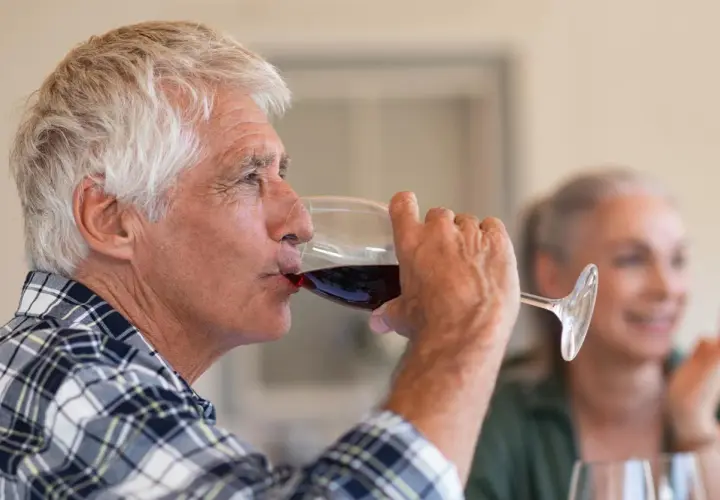 Un homme âgé boit du vin rouge. Attention, le vin périmé présente un danger.