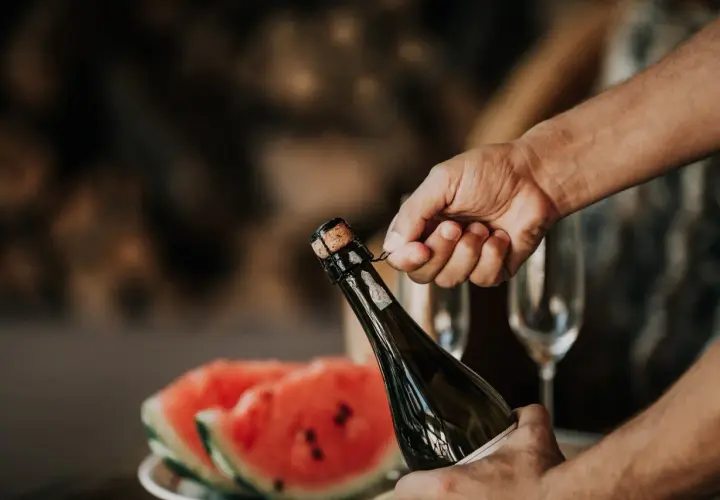 Main tenant du goulot, une main dépose délicatement le muselet. La clé pour savoir comment ouvrir une bouteille de champagne est dans ce geste précis.