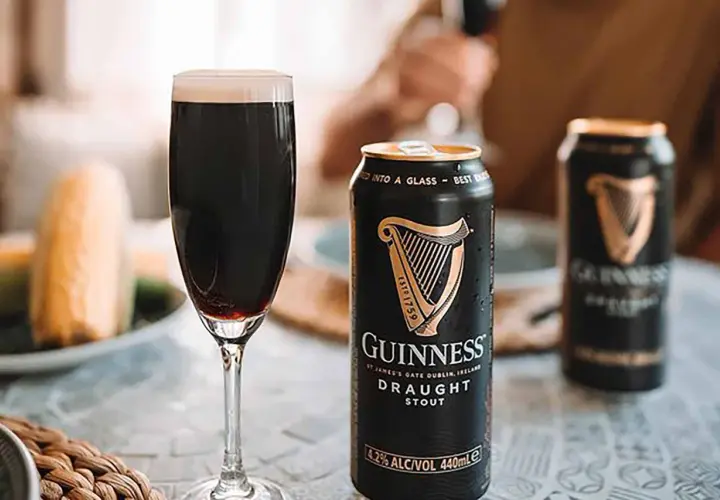 Une pinte de Guinness Draught Stout, avec son degré alcool de 4.2%, est servie à côté de canettes.